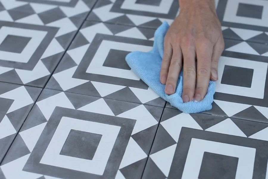 Closeup of a black and white patterned cement tile floor and a hand cleaning it with a soft blue cloth.