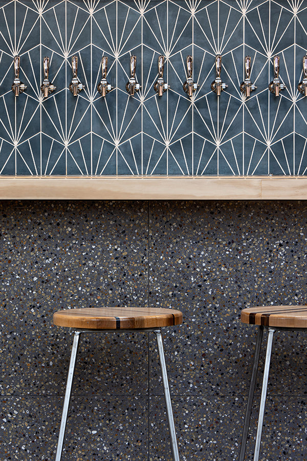 Bar area with charcoal colored terrazzo tile on lower wall and blue patterned cement tile on upper wall.