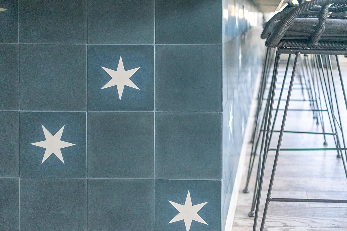 Closeup of blue cement tile with white stars on the lower wall underneath a bar.