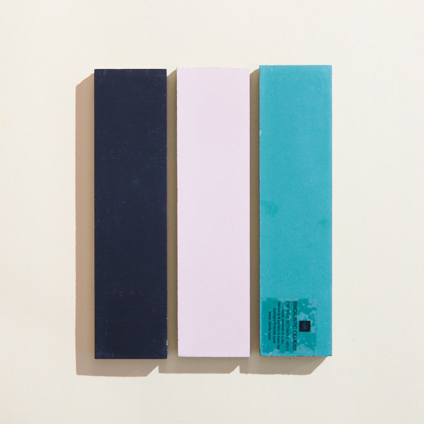 Three rectangular cement tiles in black, pink, and teal, laid vertically against a light background.