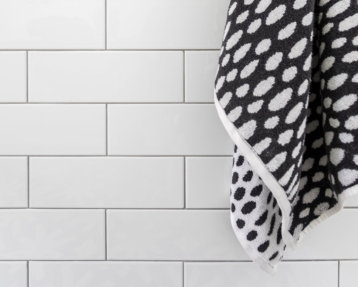 Closeup of bathroom wall tiled with glossy white rectangular subway tile.