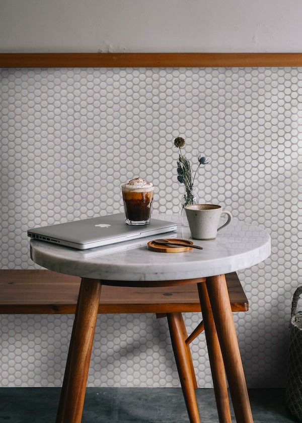 Cafe with white penny tile wall, wooden bench, and marble bistro table with coffee on top.