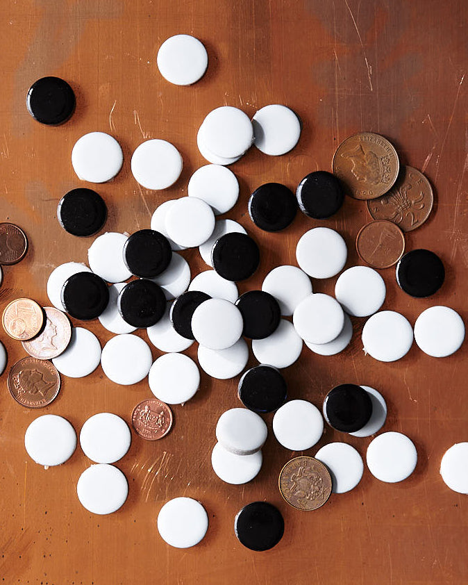 Black and white porcelain ceramic penny round tiles against dark wood background.