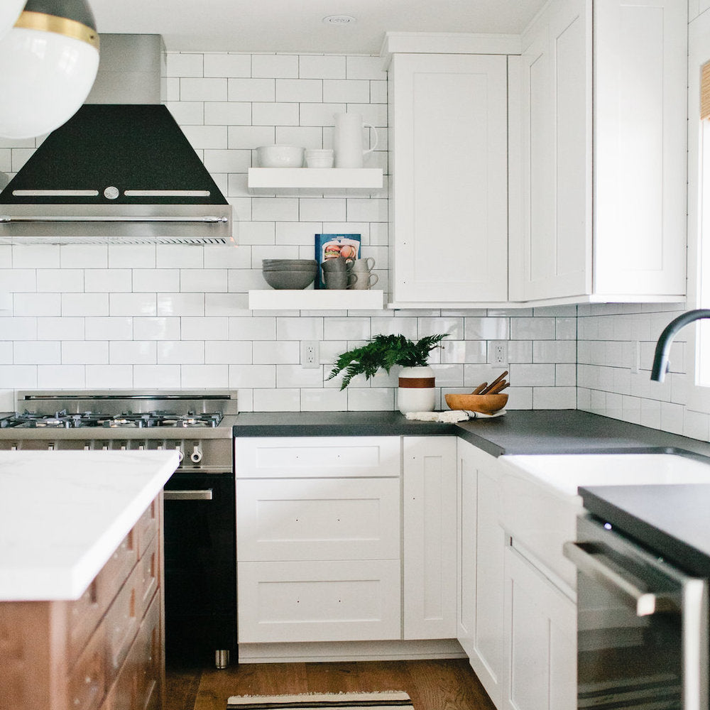 kitchen view of white subway tile backsplash, white cabinets, sink, dishwasher, black range hood