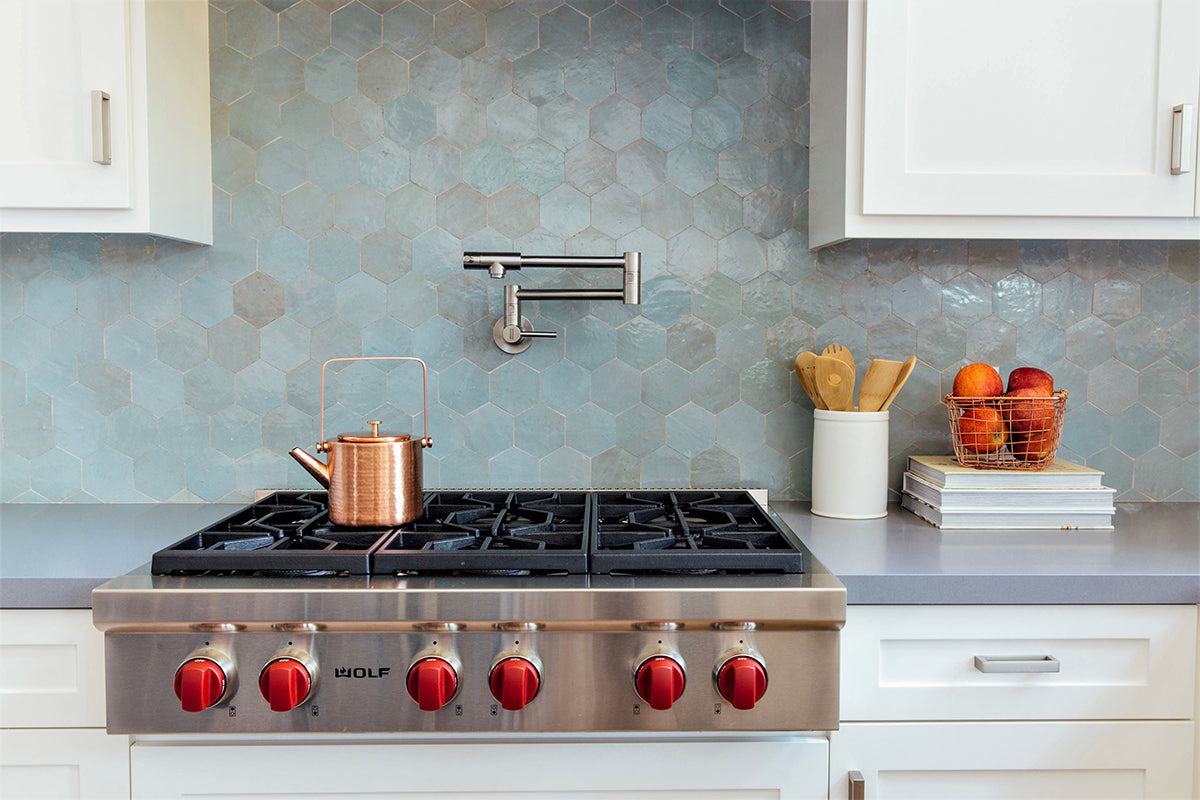 Kitchen stove area with bluish grey hexagon zellige tile backsplash and white cabinets.
