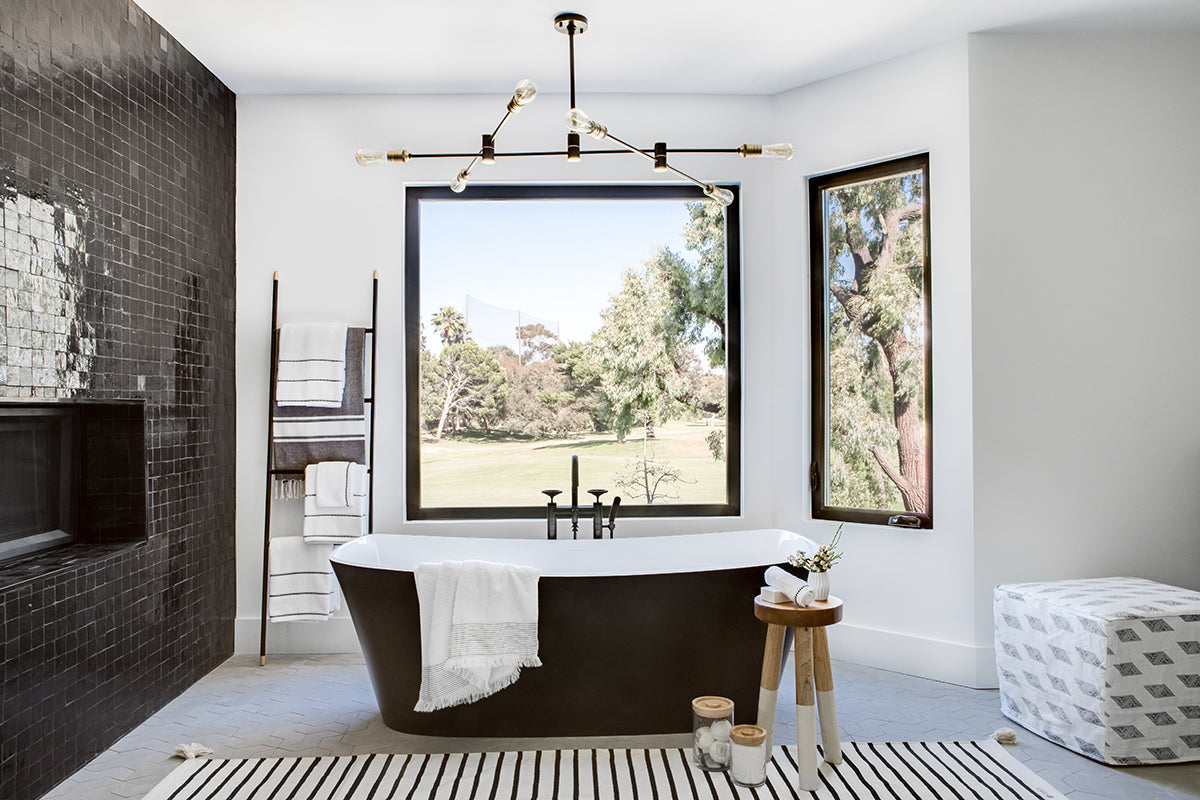 Modern black and white bathroom tub area with black bath tub and black zellige fireplace surround to the left.