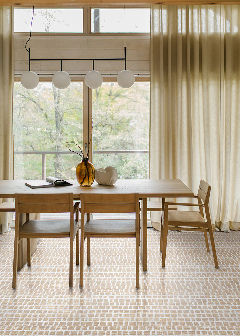 Sunlit dining room with wooden table, beige sheer curtains, and a tan rough cut mosaic tile floor.