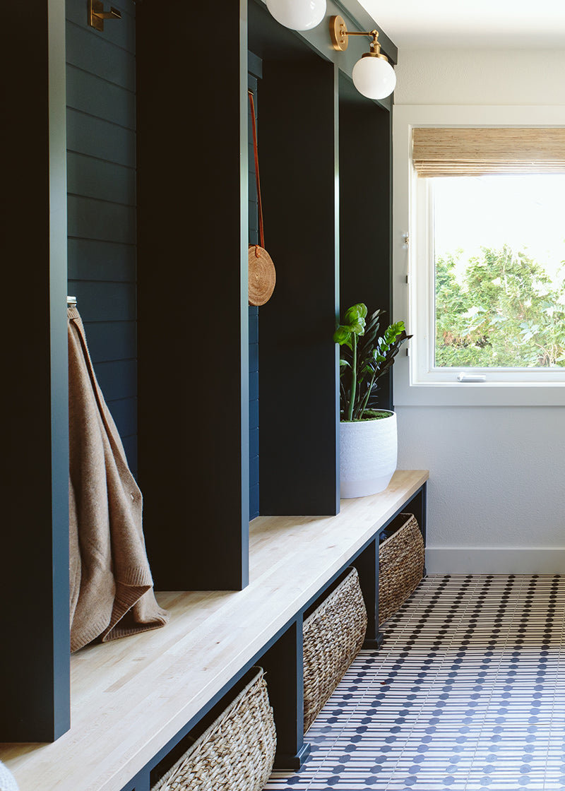 Mudroom with blue painted walls, brass hardware, and a black and white patterned cement tile floor.