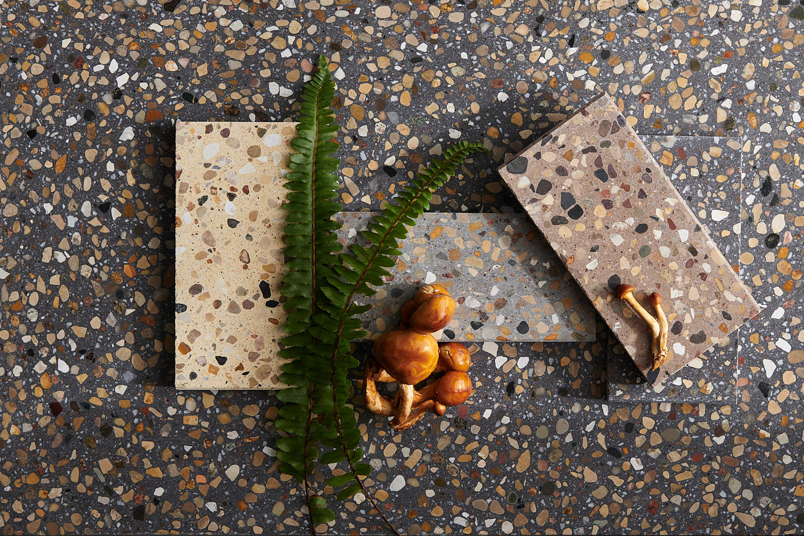 Closeup of charcoal terrazzo surface with 3 rectangular terrazzo tiles in different light brown shades on top.