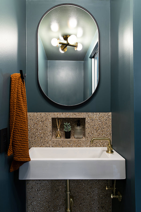 White sink in a dark blue painted modern bathroom with a tan terrazzo tile backsplash.