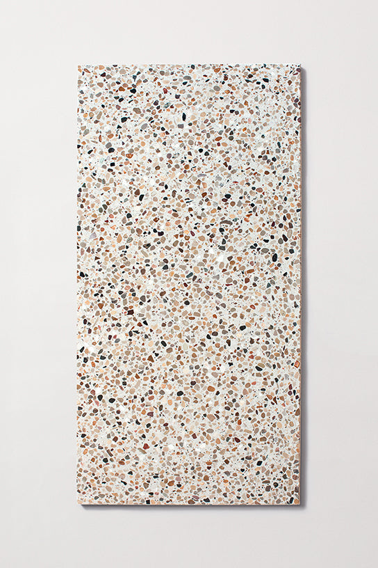 White rectangular terrazzo tile with brown and black stone pieces against a white background.