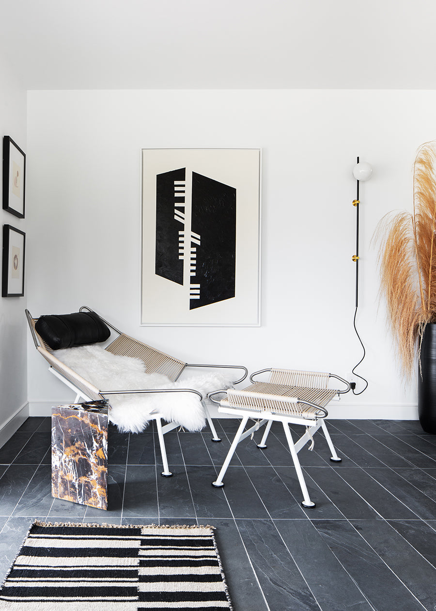 Sunlit living room with white walls, slate floor tiles, and a modern lounge chair.