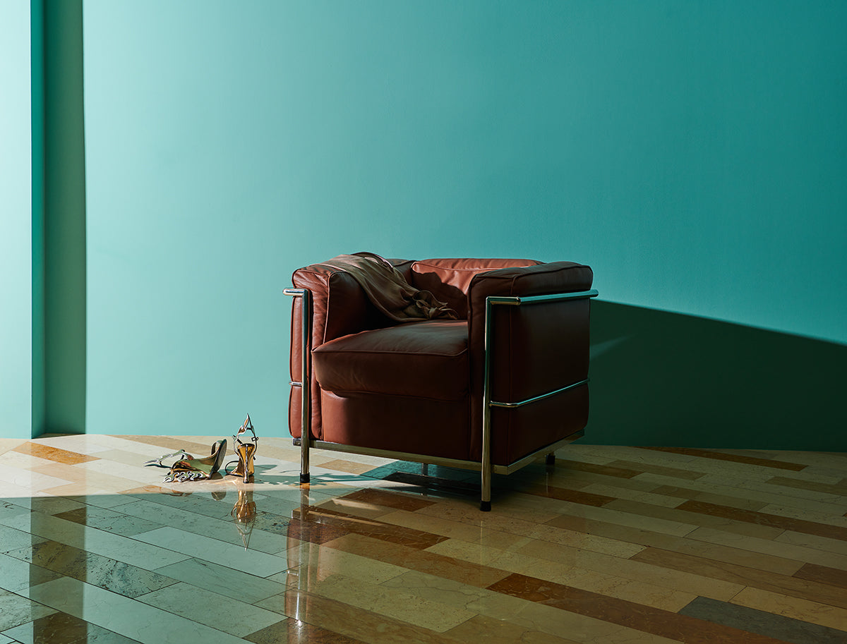 Turquoise walled space with a puffy red leather chair casting a shadow over a varied stone tile floor.