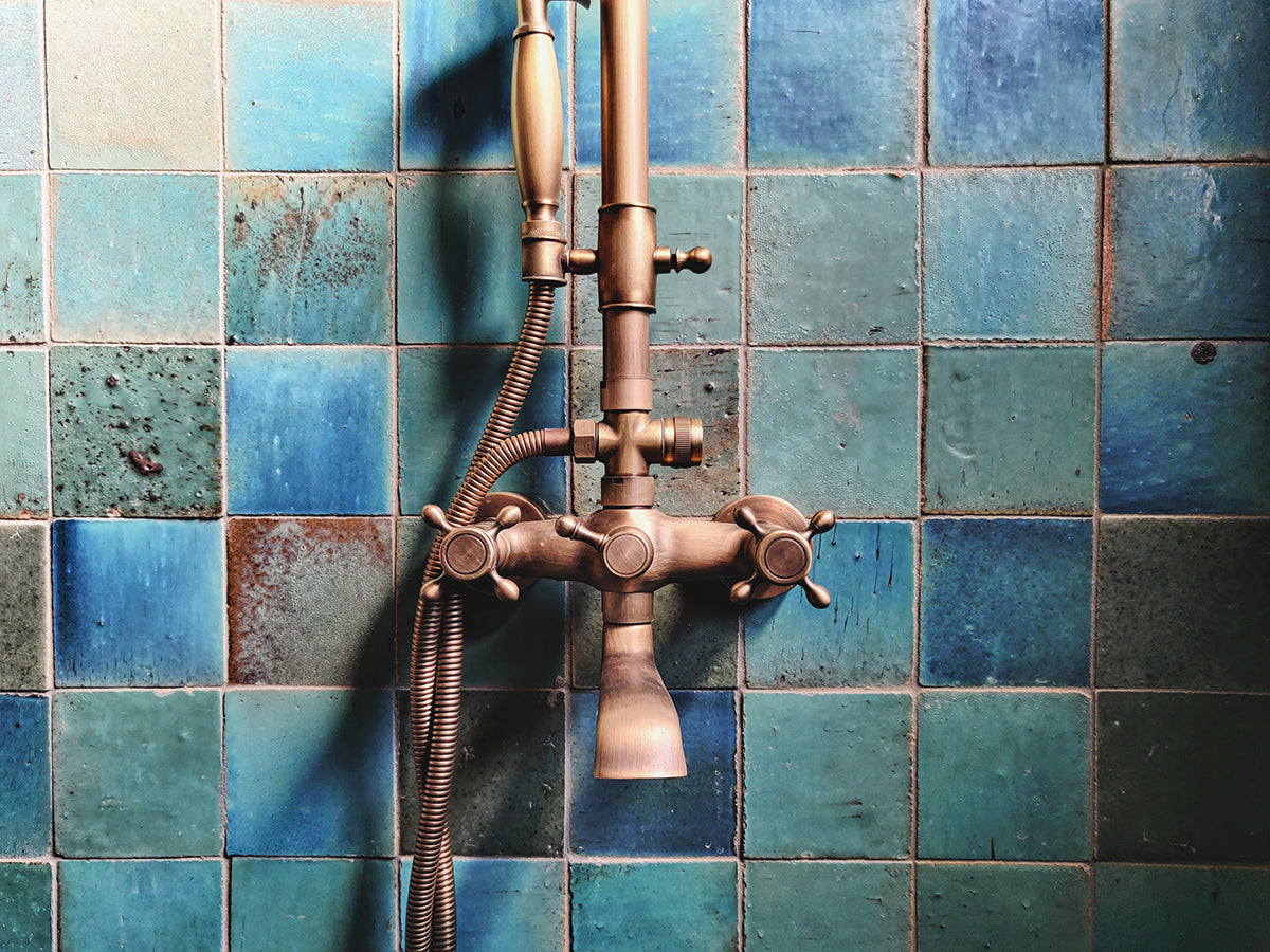 Handmade green and blue square tiles behind a shower faucet.