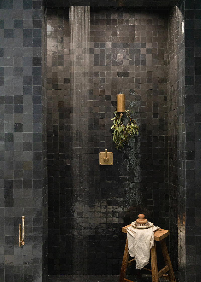 Black shower area with zellige tile along the full wall and a stool in the corner.