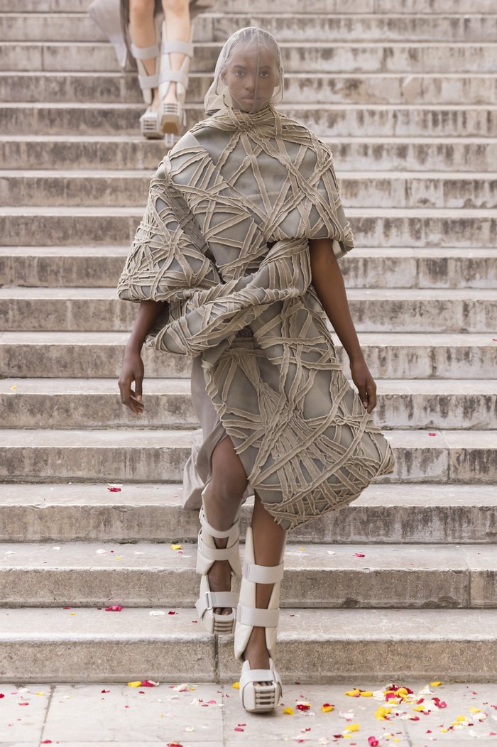 A runway look with braces as shoes and a heavily textured blanket worn as a dress with a mosquito net veil.
