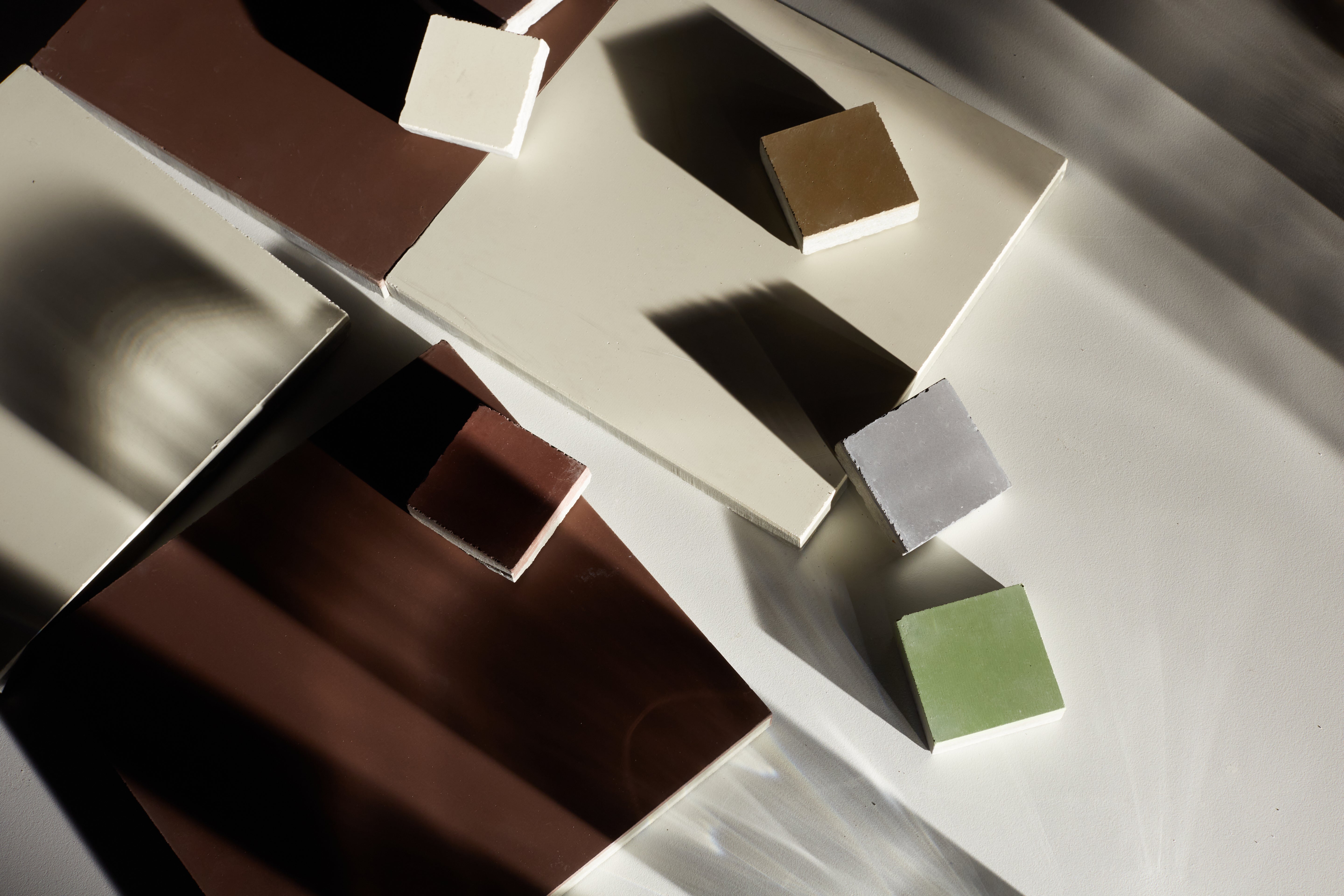 Shadowy, stylized shot of various square cement tiles in brown, cream, and light green against a white background.