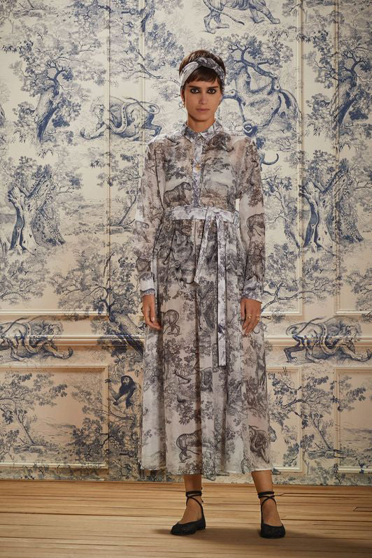 A model wears a toile dress in front of a matching wall.