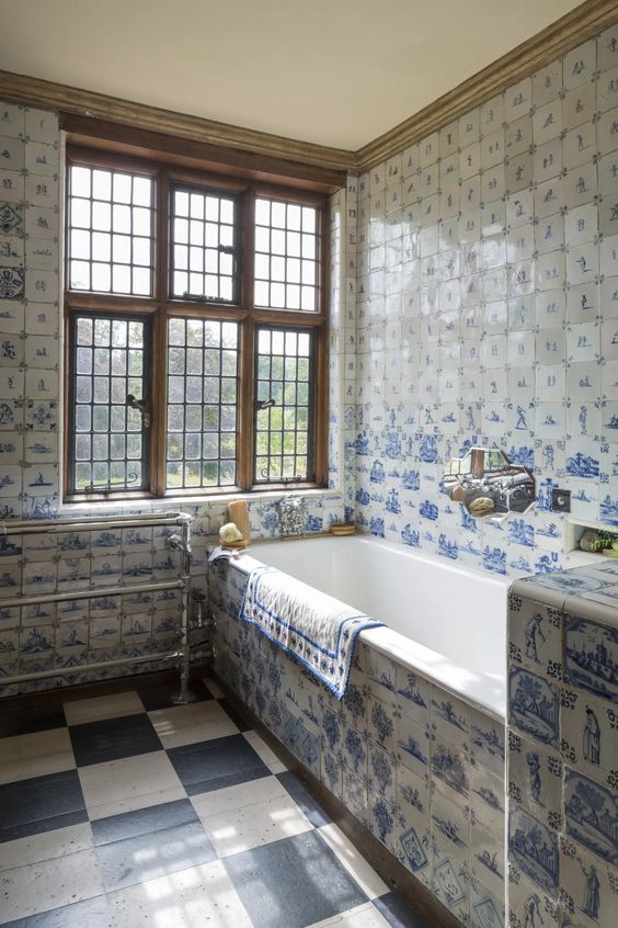 The front of a bathtub and bathroom walls covered in delft tiles.