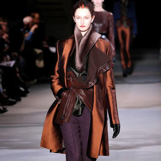 a fashion show runway model wearing a shiny coat and tweed pants