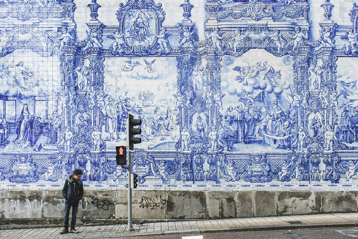 A large and elaborate azulejo mural, contrasting with a grey concrete sidewalk.