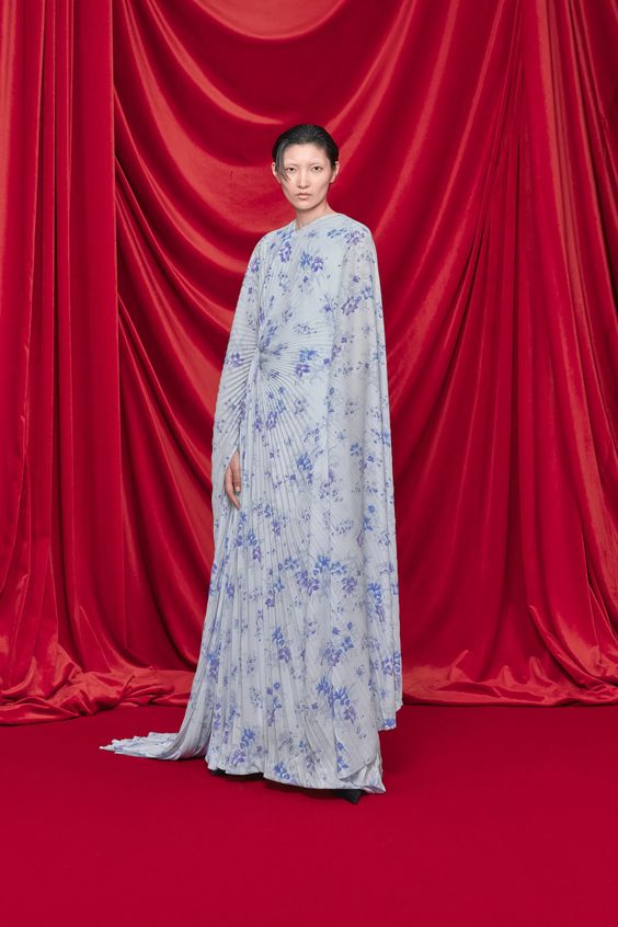 woman posing wearing floral floor length dress with a red curtain background