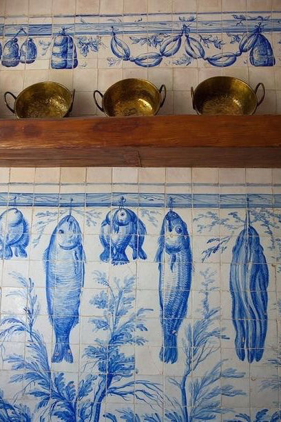 Tiles in a kitchen depict fish and sausages drying on a rack.