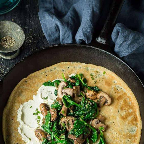 a crepe in a cast iron pan topped with mushrooms and greens