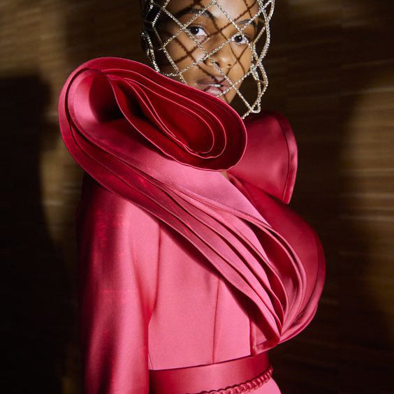 a runway model wearing a high fasion sculptural rose colored dress.