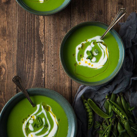 bright green soup with decorative drizzles of cream and green oil.