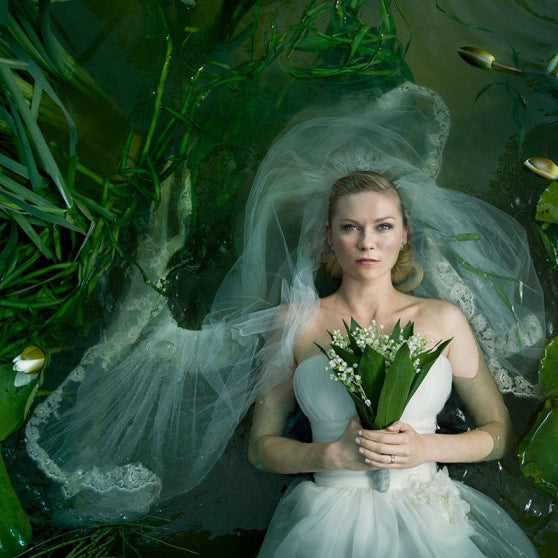 kirsten dunst floats in a pond, holding a bouquet in a wedding dress