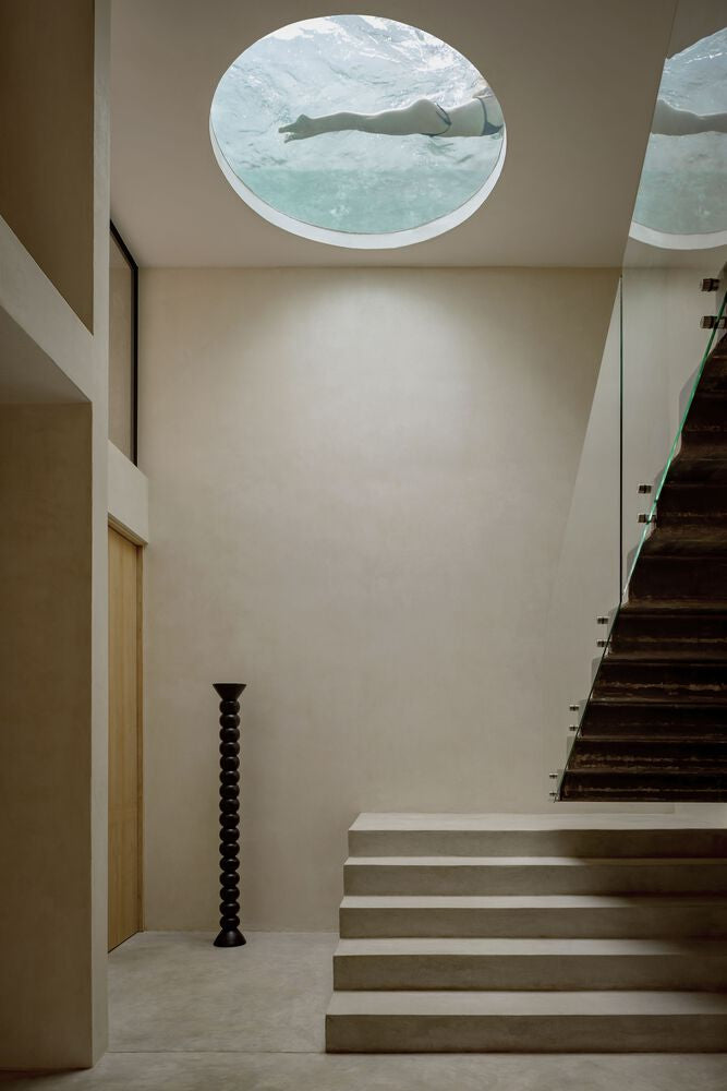 A minimalistic room with stairs and a circular cut out revealing the bottom of a pool.