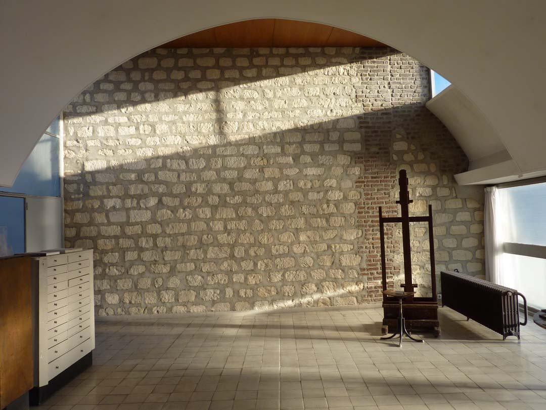 A wall with a large arch, in front of a rough stone wall with large joints and a large easel in Corbusier's studio apartment in Paris.