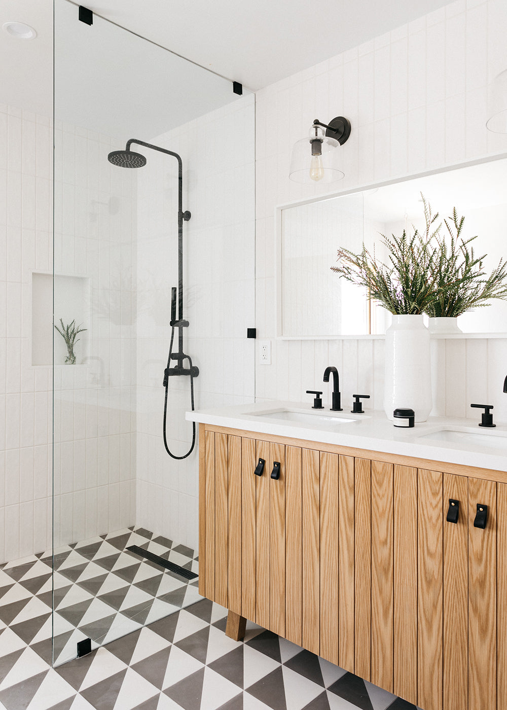 A bathroom with white tile walls, wood cabinet, black fixtures and a clé cement tile floor in black and white triangles.