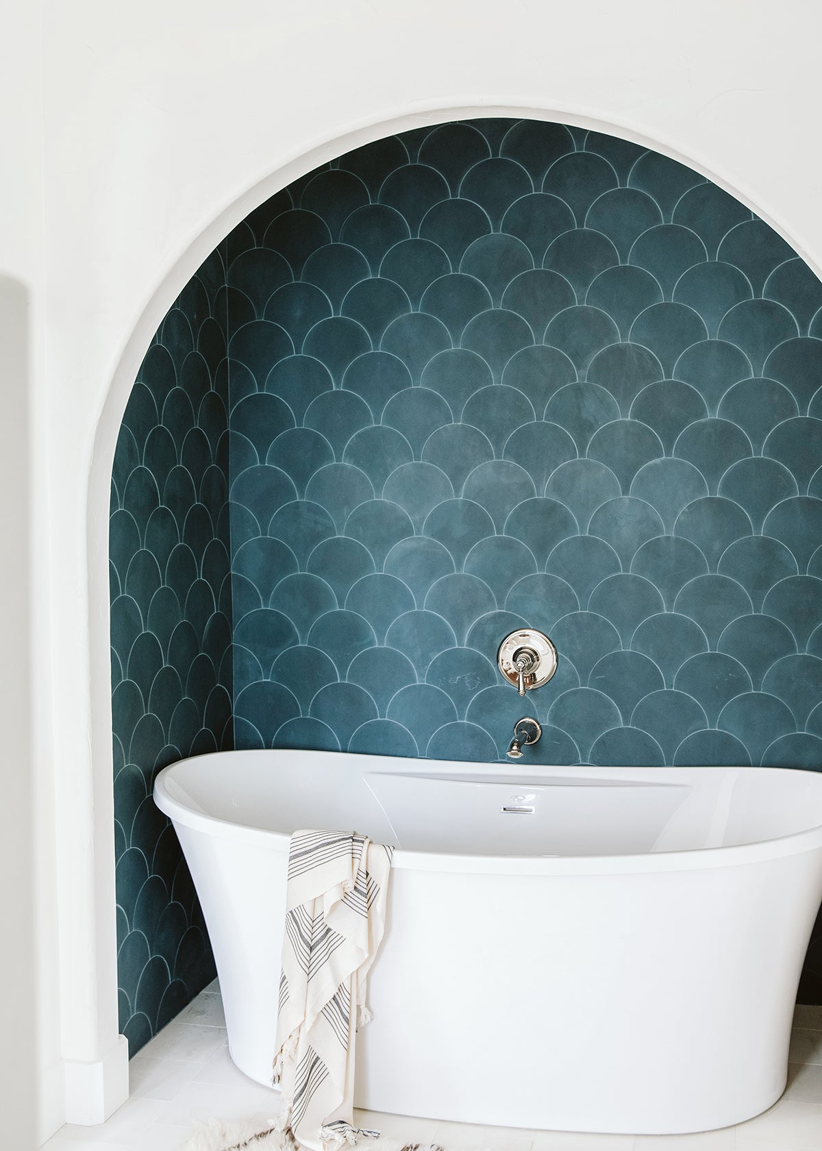 Standalone bathtub in an arched alcove in turquoise clé scalloped tiles.