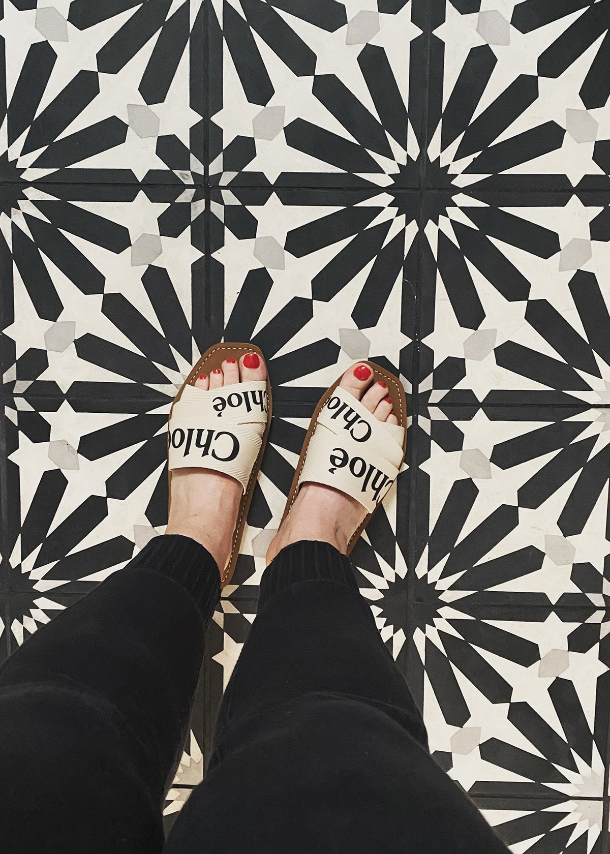 Looking down at Chloé slide sandals on a geometric cement tile floor by Clé.