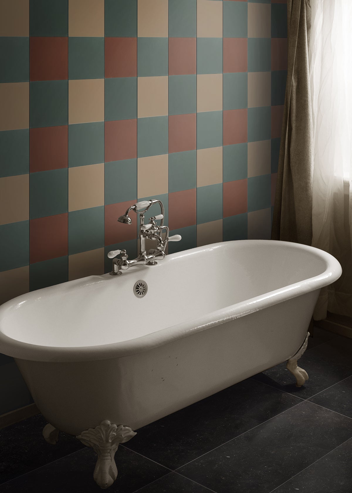 A standalone bathtub in front of large square cement tiles on a wall in a plaid-like pattern.