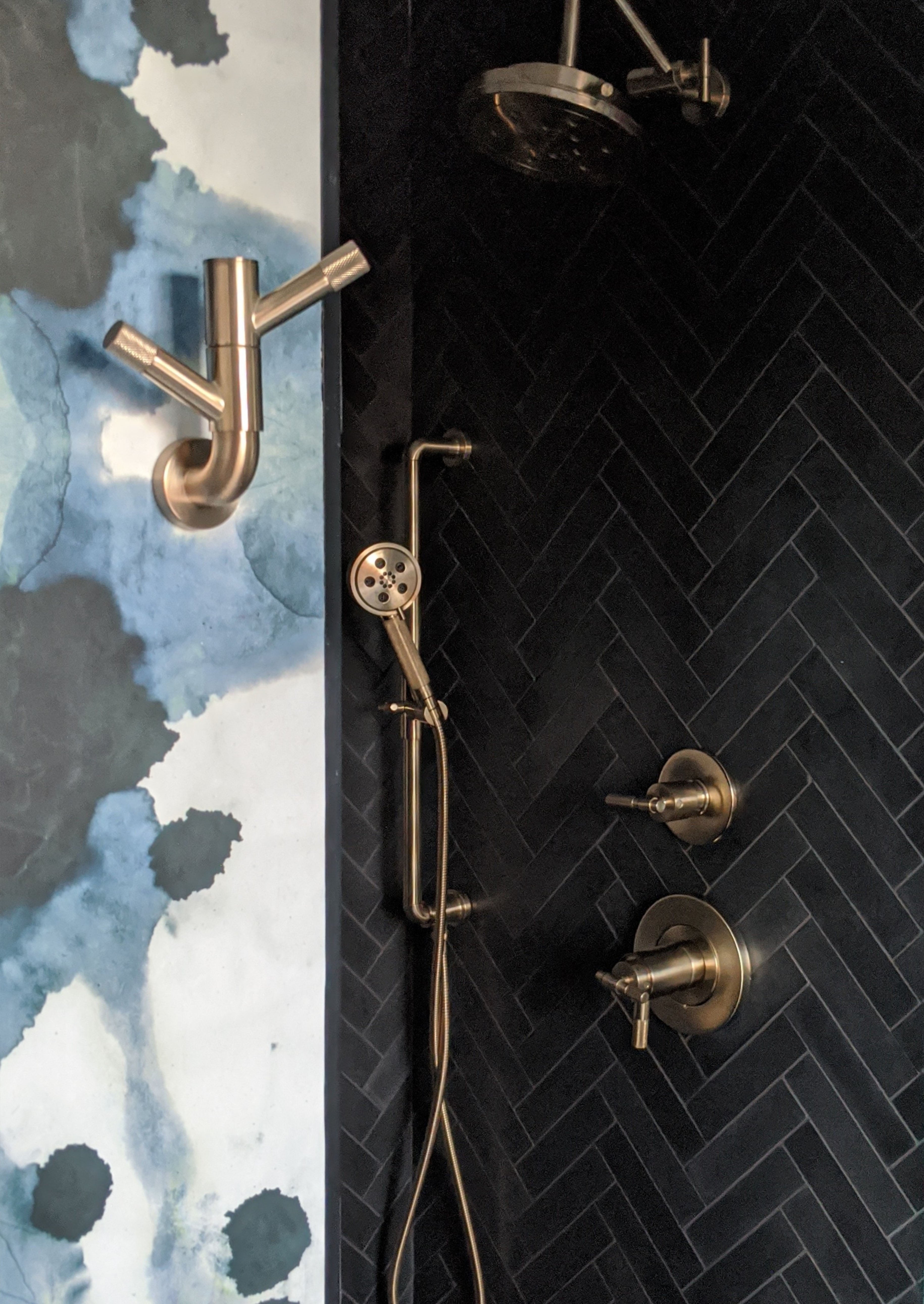 A shower wall with black rectangular tiles and a blue, white and black watercolor wallpaper wall.