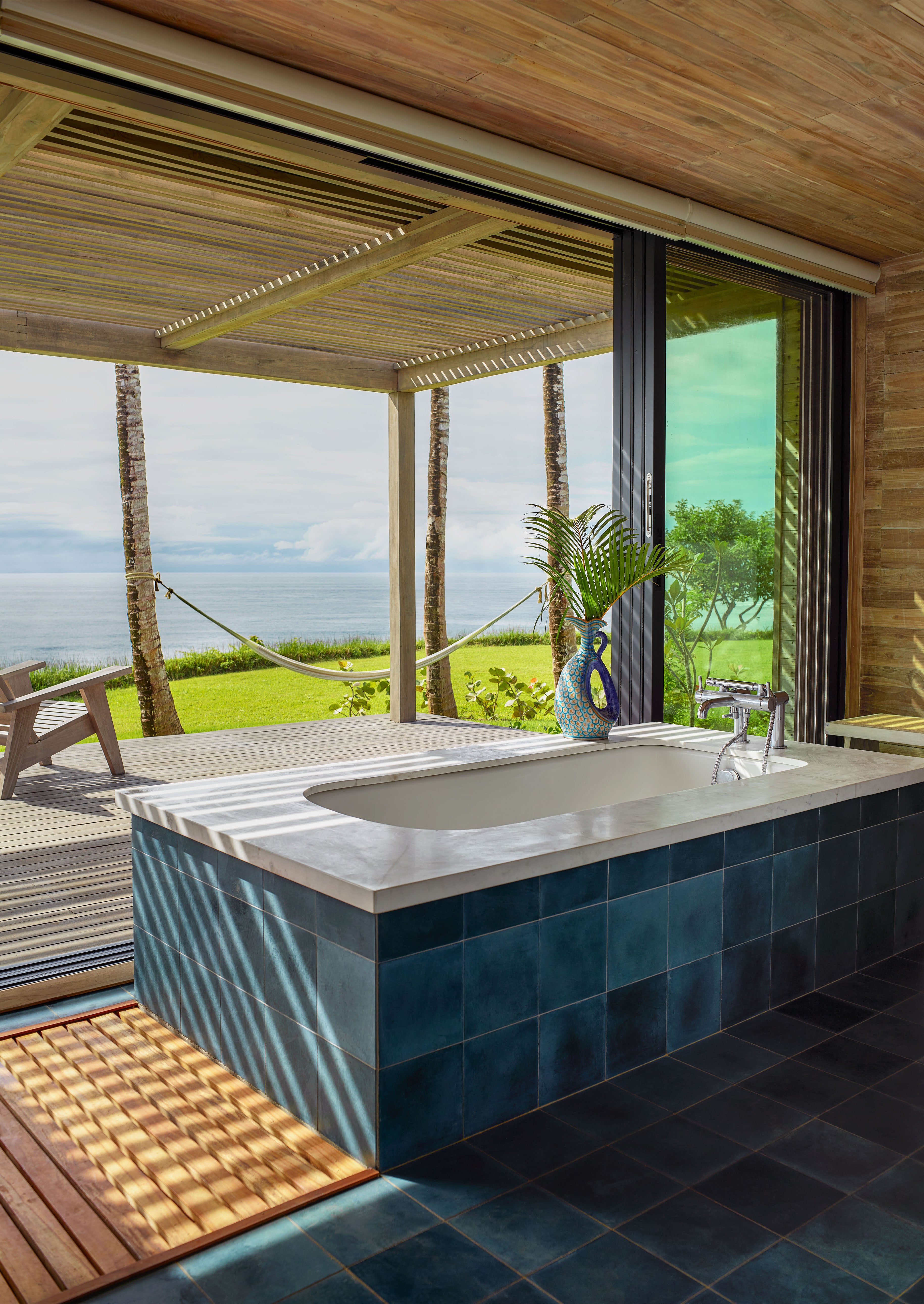 Square cement tiles in bright blue around a bathtub in a tropical home.