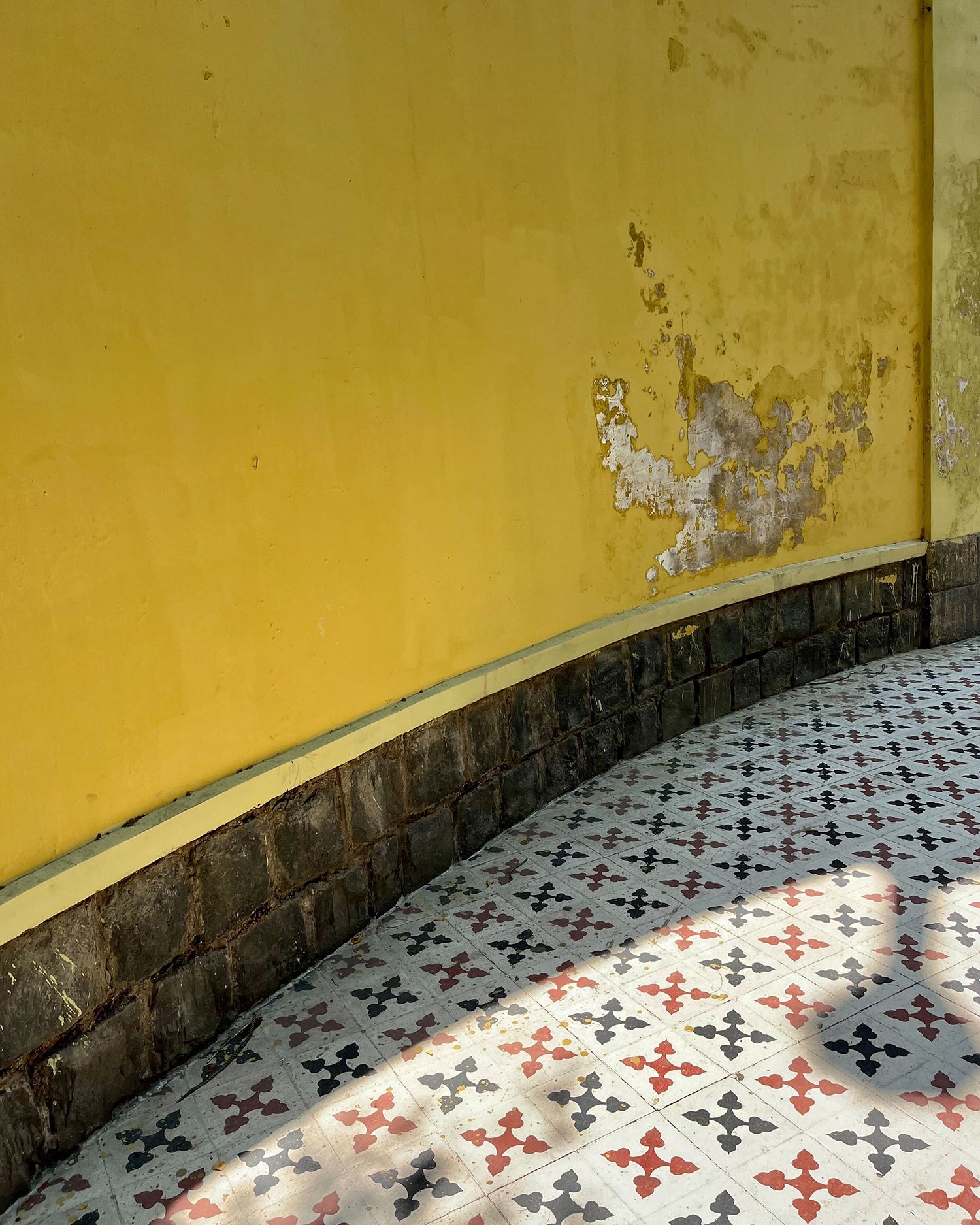A bright yellow wall above a tile floor with a navy, red and white pattern.