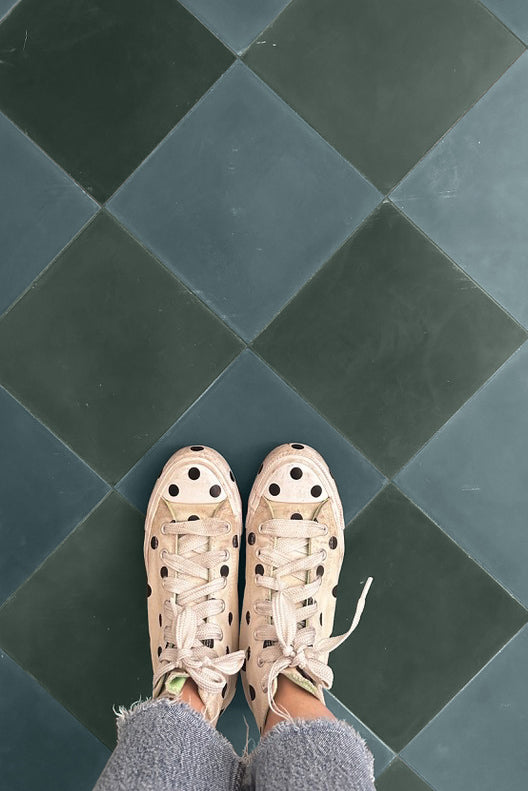 Looking down at polka dot shoes on a teal cement tile floor.