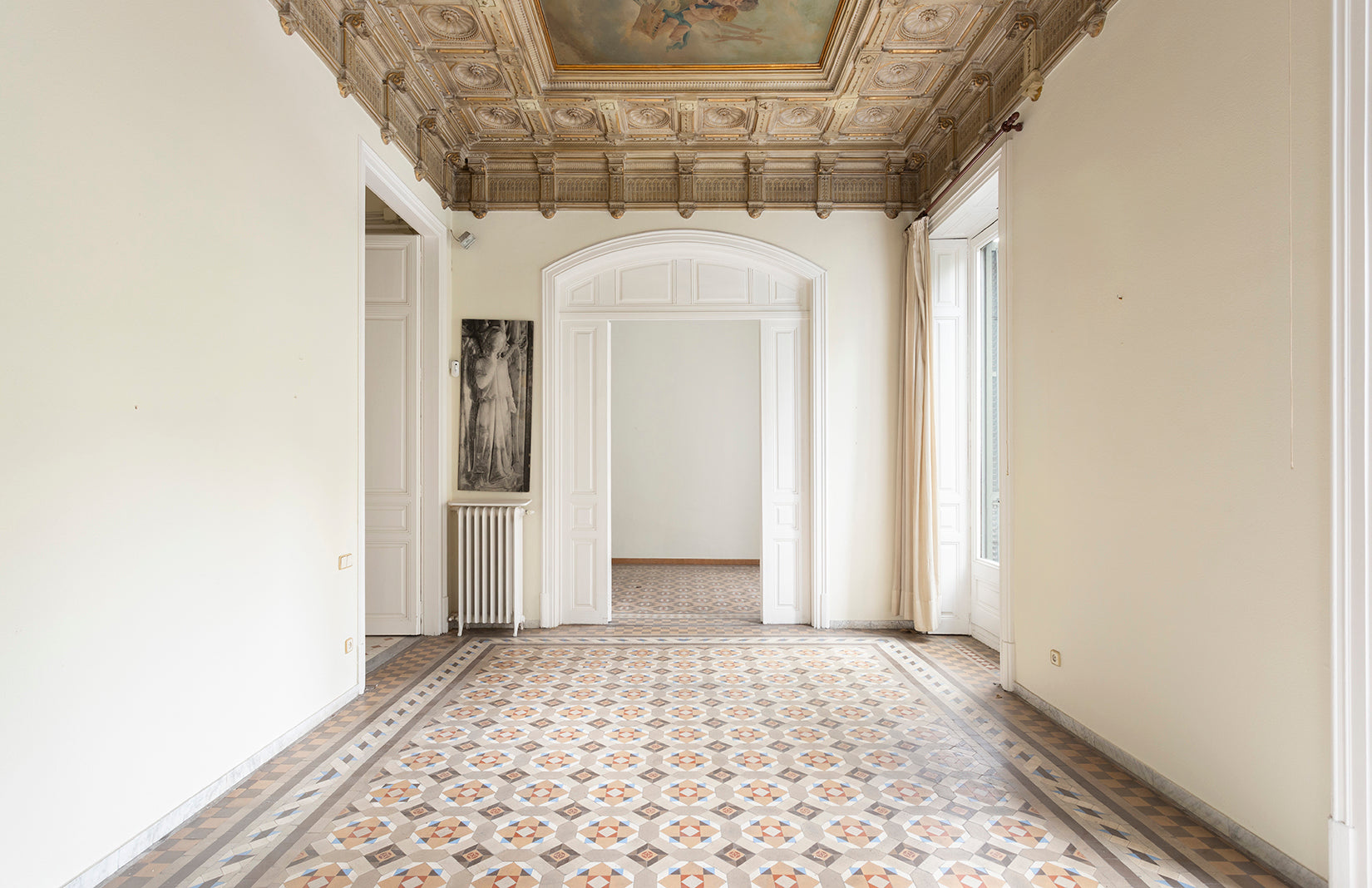 An apartment with an ornate ceiling, white plaster walls and a neutral cement tile floor.