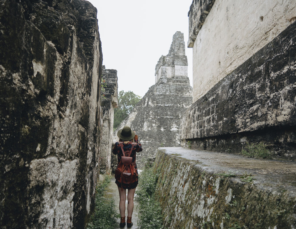 A photo of Alyssa getting ready to hike up some of the ruins and wearing a green wide brim hat, a leather backpack, and a floral mini dress.