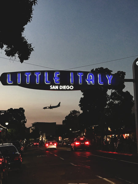 A nighttime glance into the Little Italy neighborhood of San Diego, full of lights and an airplane landing in the background