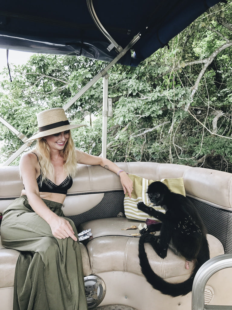 A girl with blonde hair in a wide brim Panama hat playing with a monkey on a boat