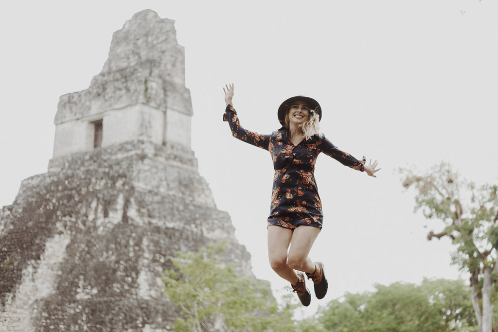 A photo of Alyssa getting ready to hike up some of the ruins and wearing a green wide brim hat, a leather backpack, and a floral mini dress.