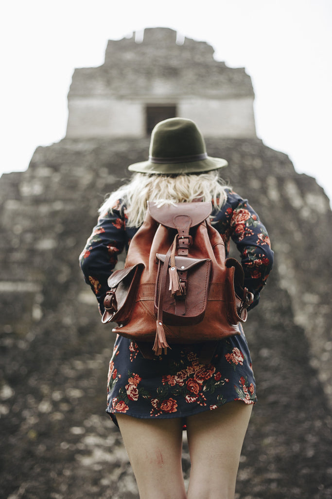 A photo of Alyssa getting ready to hike up some of the ruins and wearing a green wide brim hat, a leather backpack, and a floral mini dress.
