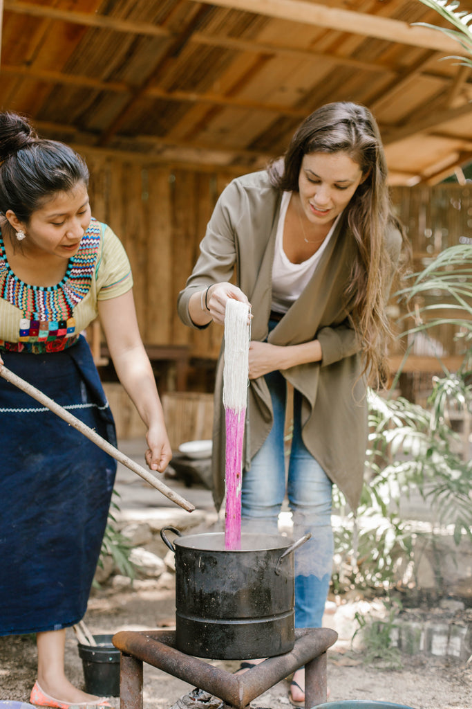 She Is Not Lost blogger Carina Otero dips strand of fabric into pot of boiling ingredients to dye it a beautiful bright pink, ethical travel bloggers, things to do in Lake Atitlan, artisan home visits Guatemala, weaving workshops in Guatemala