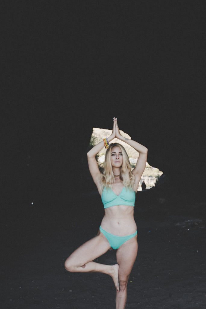 Alyssa in a yoga pose in front of a cove in a sea foam bikini 