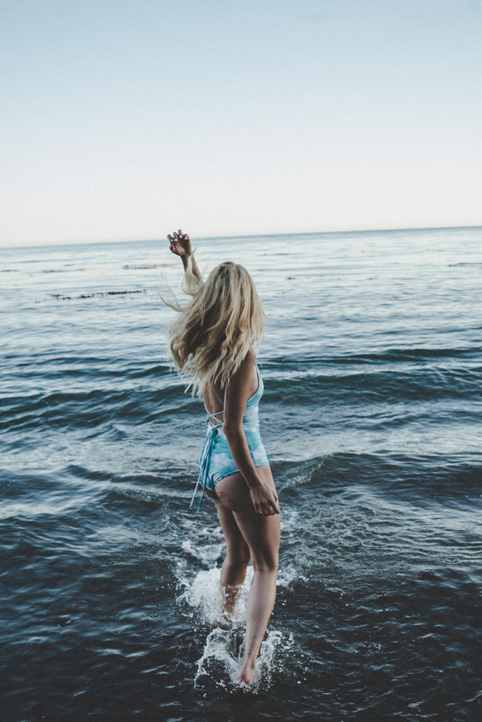 Alyssa facing the ocean wearing a blue and white tie-dye one piece swimsuit.